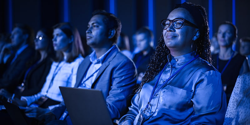 Conference attendees listen to a presentation in a dark room